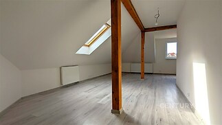 Podkrovní prostor s dřevěnými trámy, světlá laminátová podlaha, střešní okno. Moderní design a čisté linie, ideální pro útulné bydlení.