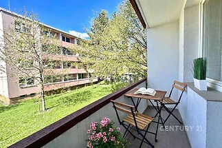 Zasklený balkon s výhledem na zeleň, dlažba a moderní terasa, ideální pro relaxaci a venkovní posezení