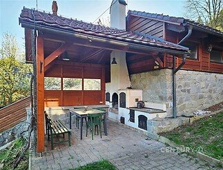 Kryté venkovní posezení s krbem, přírodní kámen a dřevěné obložení vytváří útulnou atmosféru, ideální pro posezení na zahradě