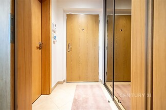 Vstupní hala s dlažbou, zrcadlovou šatní skříní a dřevěnými dveřmi. Moderní a světlý prostor nabízí praktické úložné možnosti.