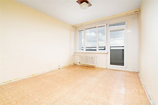 Prázdná místnost s velkými okny a balkonovými dveřmi, parketová podlaha, světlé stěny, vhodná pro rekonstrukci nebo modernizaci prostoru.