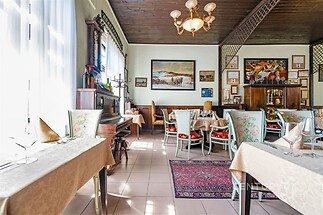 Restaurace s klasickým interiérem, dřevěným stropem a velkými okny, nabízí útulnou atmosféru a dekorativní koberec.