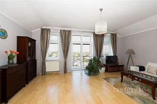 Prostorný obývací pokoj s parketovou podlahou a velkými okny, které zajišťují světlý interiér, moderní dekor s elegantním nábytkem.