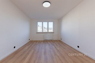 Světlý pokoj s parketovou podlahou a velkými okny, nabízející moderní atmosféru a výhled na okolní krajinu.