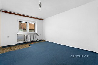 Prostorná ložnice s modrým kobercem, velkým oknem a bílými stěnami, ideální pro rekonstrukci dle vlastního stylu.