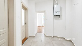 Chodba s dlažbou a bílými stěnami, moderní plynový kotel, dveře vedou do prostor s parketovou podlahou, světlý interiér.