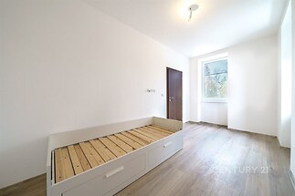 Ložnice s parketovou podlahou, velkým oknem a vestavěným lůžkem, moderní a světlý interiér vhodný pro flexibilní využití