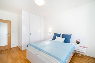 Prostorná ložnice s parketovou podlahou, vestavěné skříně a moderní minimalistický design, ideální pro komfortní bydlení.