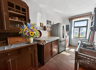 Rustikální kuchyň s dřevěnou podlahou, masivním nábytkem a velkým oknem poskytujícím dostatek světla, tradiční venkovský styl.