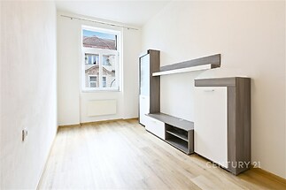Světlý obývací pokoj s velkými okny, parketovou podlahou a moderním nábytkem, ideální pro útulné bydlení.