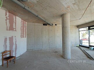 Prázdný komerční prostor s betonovými stěnami, velkými okny a moderním designem, ideální pro kancelář nebo obchod.