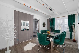 Jídelna s moderním designem, luxusní zelené čalounění, tmavá dřevěná podlaha, velká okna se závěsy, elegantní osvětlení, světlý interiér.