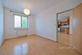 Světlý obývací pokoj s parketovou podlahou, velkými okny a moderním designem, navazuje na kuchyňský prostor v rekonstruovaném stavu.