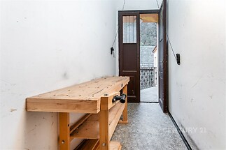 Úzká chodba s dřevěným pracovním stolem, vede na balkon s výhledem. Vinylová podlaha, světlý prostor, ideální pro kutilské práce.