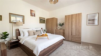 Prostorná ložnice s moderním nábytkem, světlým kobercem a vestavěnými skříněmi. Elegantní dekorace a přírodní světlo vytvářejí útulnou atmosféru.