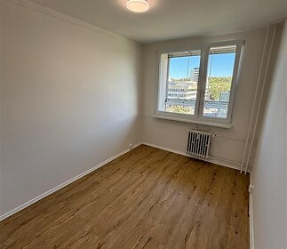 Světlý pokoj s dřevěnou podlahou, moderním stylem a velkými okny.