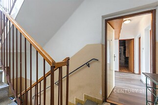 Vstupní prostor s parketovou podlahou a dřevěným zábradlím, vedoucí do bytu, který nabízí moderní design a světlé interiéry.