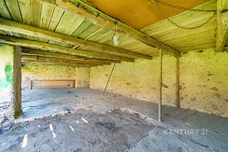 Prostorná rekonstrukční místnost s kamennými zdmi a dřevěným stropem, ideální pro renovaci a přeměnu na obytný prostor.