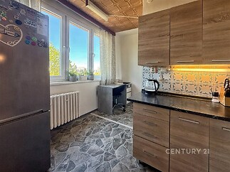 Kuchyň s moderní dlažbou, dřevěnými skříňkami a velkými okny poskytuje světlý prostor.