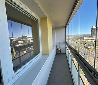 Prostorný balkon s dlažbou a proskleným zábradlím nabízí panoramatický výhled na město, což zajišťuje moderní a světlé venkovní prostředí.