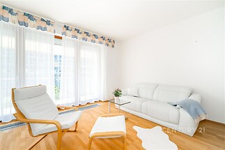 Světlý obývací pokoj s parketovou podlahou, velkými okny a moderní sedací soupravou vytváří příjemný a vzdušný prostor.