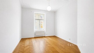 Světlý obývací pokoj s parketovou podlahou, velké okno a bílými stěnami, moderní design a vysoké stropy poskytují prostornost