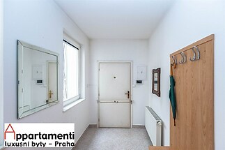 Vstupní hala s dlažbou, bílými stěnami a velkým oknem nabízí dostatek přirozeného světla. Praktické úložné prostory s věšáky na kabáty.