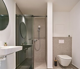 Moderní koupelna s dlažbou, prosklený sprchový kout a minimalistický design, elegantní umyvadlo a závěsné WC pro svěží vzhled.