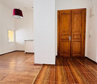 Světlá chodba s dřevěnými dveřmi, parketovou podlahou a moderním osvětlením, v předsíni je vidět část bílé kuchyně