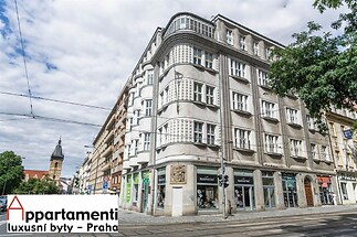 Historická budova s členitou fasádou, nacházející se na rohu rušné ulice v městské části, s obchodními prostory v přízemí.