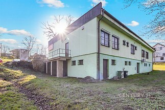 Průmyslová budova s plechovou střechou a velkými okny na travnatém pozemku, vhodná pro komerční využití nebo skladování.