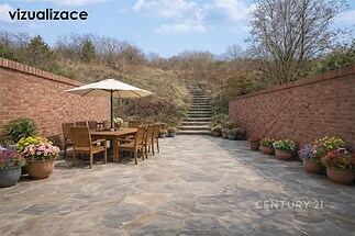 Prostorná venkovní terasa s kamennou dlažbou, obklopena cihlovými zdmi, vybavena dřevěným nábytkem a květinovými dekoračními prvky.