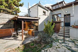 Dvůr s kamennou dlažbou a venkovním posezením, cihlová zeď a vzrostlé stromy tvoří útulné prostředí pro relaxaci venku.