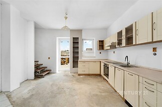 Světlá kuchyň s moderními spotřebiči, vestavěnými skříněmi a velkými okny, nabízí parketovou podlahu a propojení s jídelním koutem.