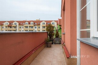 Prostorný balkon s dlažbou a moderním zábradlím nabízí výhled na okolní zástavbu, ideální pro relaxaci a venkovní posezení.