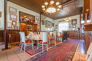 Prostorná jídelna s dřevěným stropem, dlažbou a zdobeným kobercem, stůl pro osm osob, elegantní svítidla, historický styl.