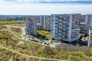 Panelový bytový komplex s moderními fasádami, obklopený zelenými plochami a parkovištěm, nabízí klidné bydlení na okraji města.