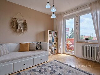 Světlý obývací pokoj s parketovou podlahou, velkými okny a moderním nábytkem, poskytuje pohodlný prostor ve stylu skandinávského designu.