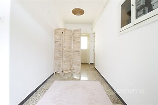 Úzká chodba s dlažbou, bílými stěnami a dekorativním dřevěným paravanem, což vytváří světlý a moderní vzhled interiéru.