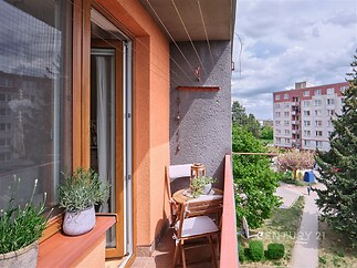 Krytý balkon s dlažbou, dřevěné zábradlí a výhled na zelený dvůr, poskytuje klidný prostor pro relaxaci, vhodný pro rostliny a venkovní posezení.