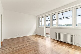 Světlý obývací pokoj s parketovou podlahou, velkými okny a výhledem na město, moderní styl a příjemná atmosféra.