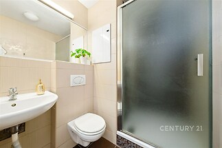 Kompaktní koupelna s matným sprchovým koutem, světlá dlažba a moderní sanitární prvky nabízí čistý a funkční design.