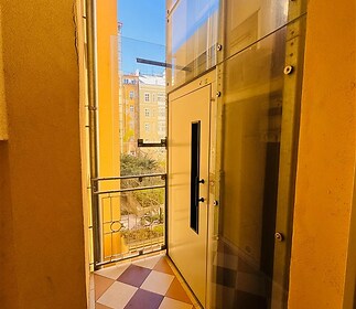 Světlá lodžie s dlažbou a skleněnými stěnami nabízí moderní design a výhled.