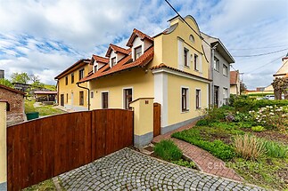 Rodinný dům s červenou střechou a žlutou fasádou, kamenná příjezdová cesta, udržovaná zahrada, klidná rezidenční oblast