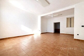 Světlý obývací pokoj s dlažbou, velká okna a moderní bílý strop s ventilátorem, ideální pro prostorný interiér.