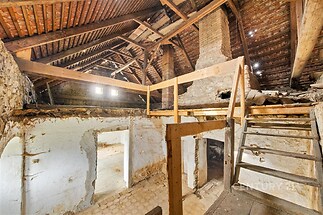 Podkrovní prostor s dřevěnými trámy, cihlovými zdmi a dřevěnými schody, vhodný k rekonstrukci.
