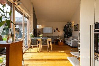 Světlý obývací pokoj s parketovou podlahou, velkými okny a moderním nábytkem. Prostorný interiér ideální pro rodinné posezení.