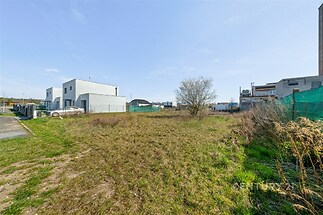 Stavební pozemek s rovinatým terénem, moderní zástavba v okolí, vhodné pro developerský projekt.