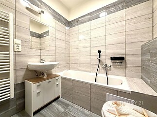 Moderní koupelna s dlažbou, vanou a umyvadlem, skříňka pod umyvadlem, koupelnový radiátor. Světlá rekonstrukce ve stylovém provedení.