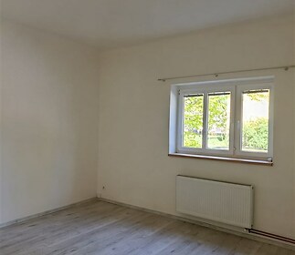 Světlá ložnice s moderní laminátovou podlahou, velkými okny a neutrálními barvami, ideální pro útulné bydlení.